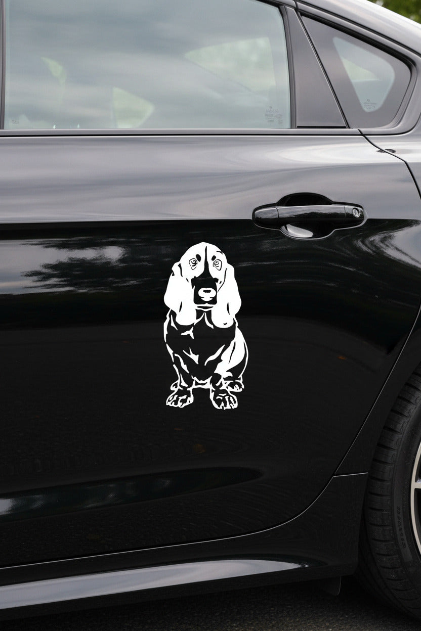 Weißer Basset Hound Aufkleber sitzend in voller Körperlänge auf einem schwarzen Auto – wetterfestes Autoaufkleber-Motiv von amberdog