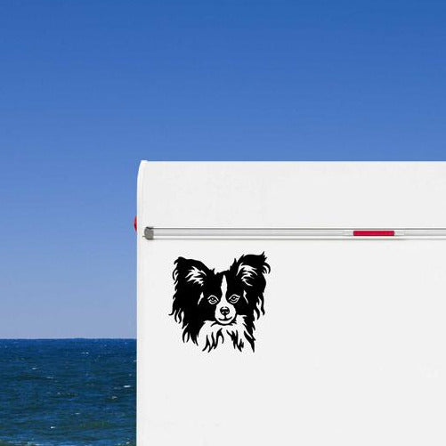 Schwarzer Papillon Spaniel Kopf Aufkleber auf der weißen Wand eines Wohnmobils am Meer, wetterfestes Autoaufkleber-Motiv von amberdog