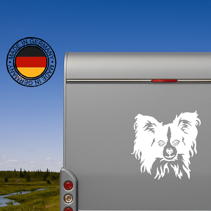 Weißer Papillon Spaniel Kopf Aufkleber auf der grauen Rückwand eines Wohnmobils vor blauem Himmel, wetterfestes Autoaufkleber-Motiv von amberdog